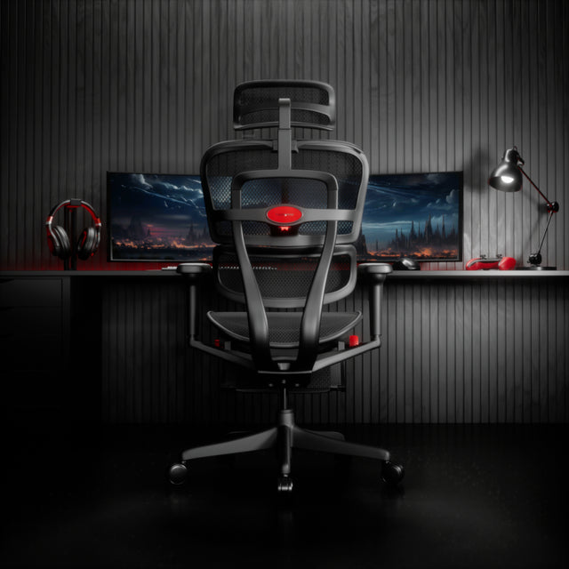 Black Ergohuman Ultra gaming chair at a desk with two monitors that showcase a virtual realm. On the desk is a pair of headphones, a controller, and a black lamp. The room is dimly lit with black flooring and black panelling.