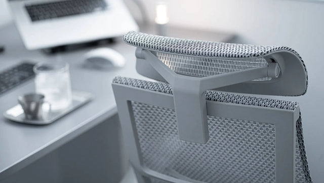 Close up of the top back of the Ergohuman Pro-Fit chair in a grey frame with grey mesh, headrest included. It's at a desk with a laptop, keyboard, and a glass of water. comfortable office chair