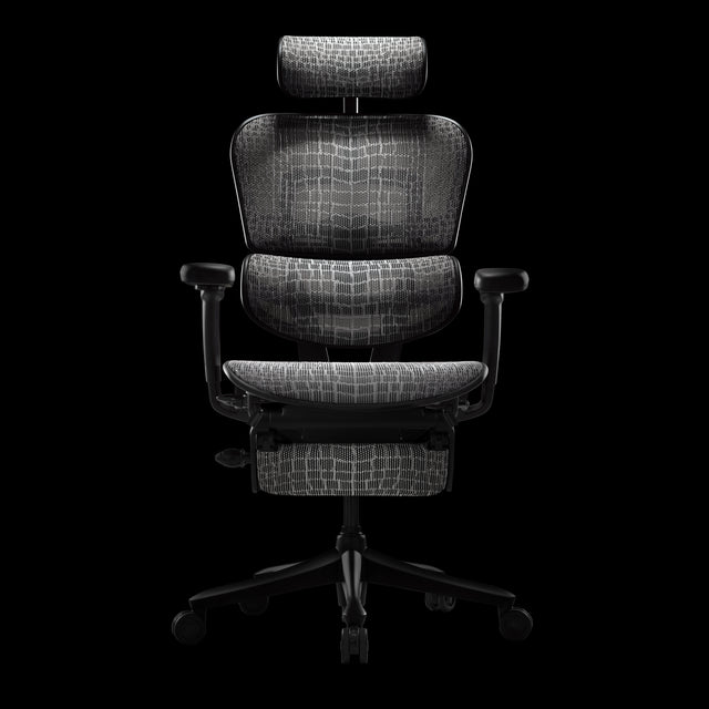 Front view of the 24-hour gaming chair, Ergohuman Carbon, in a black frame with black and grey carbon fibre detailed mesh. The chair features a headrest and legrest. It is positioned in a black studio space with a black background.